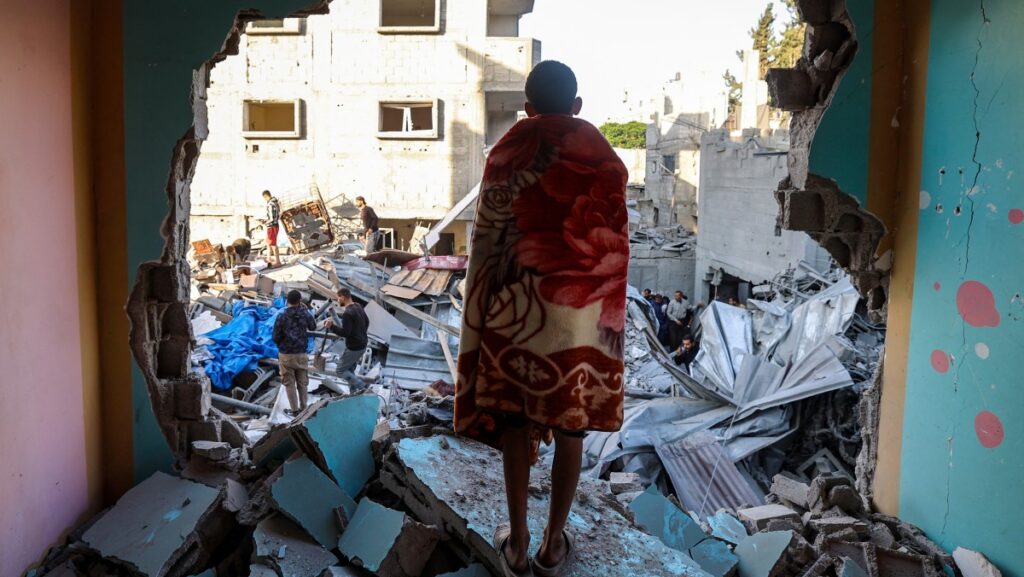 Un joven envuelto en una manta observa cómo la gente busca supervivientes entre los escombros de un edificio destruido por un ataque israelí en el campamento de refugiados palestinos de Bureij, en el centro de la Franja de Gaza, el 2 de mayo de 2025. (Foto de Eyad BABA / AFP)