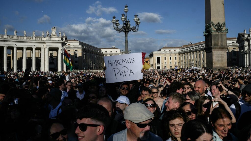 Un hombre sostiene un cartel que dice "Habemus Papa" (Tenemos un Papa) después de que una columna de humo blanco saliera de la chimenea de la Capilla Sixtina, indicando que los cardenales eligieron un nuevo papa durante su cónclave secreto, en la Plaza de San Pedro del Vaticano, el 8 de mayo de 2025. (Foto de JEFF PACHOUD / AFP)